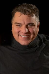 Eric Berlin smiling, in a black turtleneck — self-portrait
