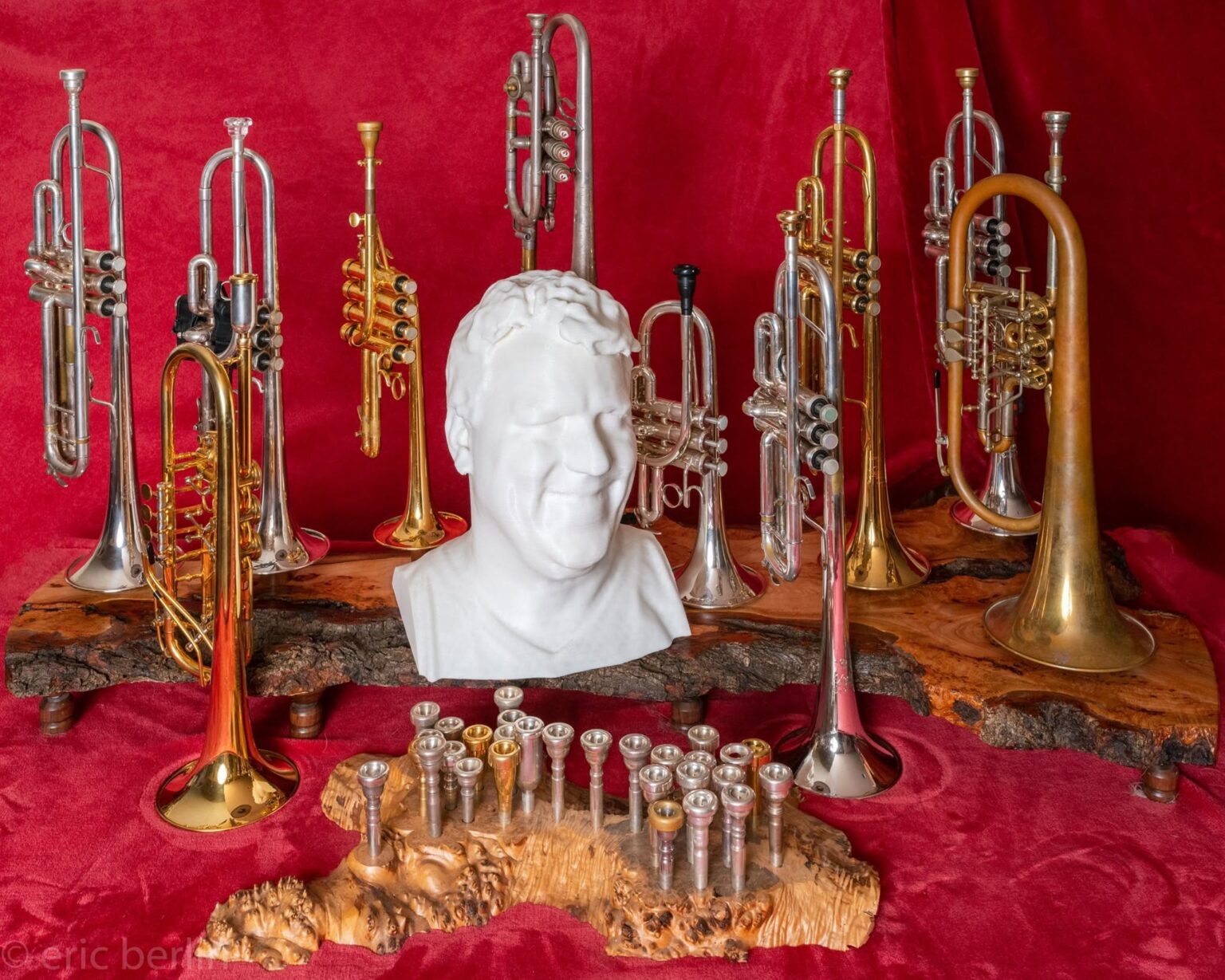 Eric Berlin’s trumpets, cornets, flugelhorns and mouthpieces displayed on live-edge wood stands around a white sculpted bust, against red velvet